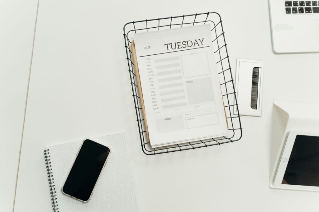 Top view of a neat office desk with a Tuesday planner, smartphone, and gadgets, perfect for scheduling and organization.
