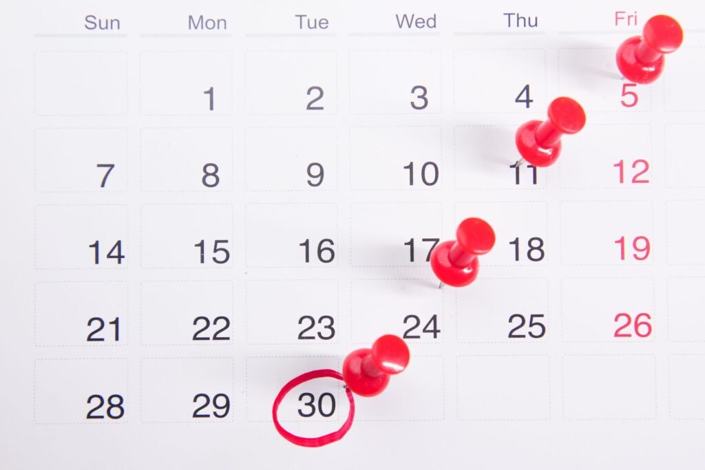 Close-up of a calendar with red push pins marking important dates, emphasizing deadlines.