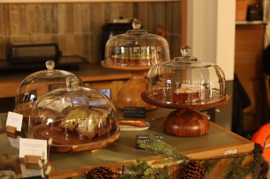 Showcase of pastries and cakes under glass domes on wooden stands in a bakery setting.