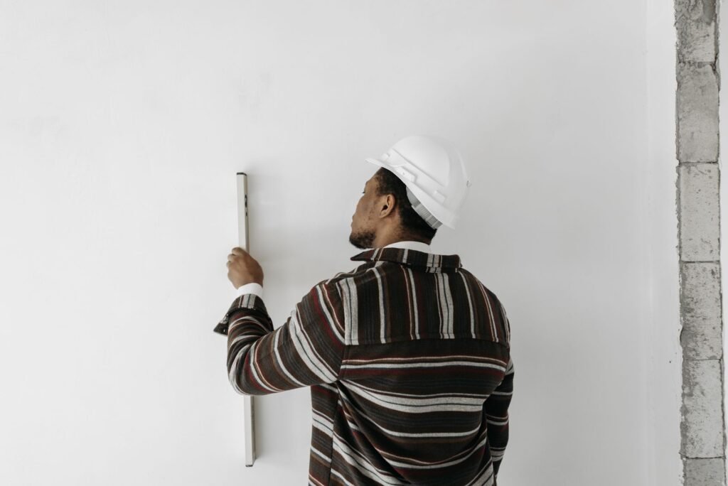 Back view of a man using a level to measure wall verticality indoors.