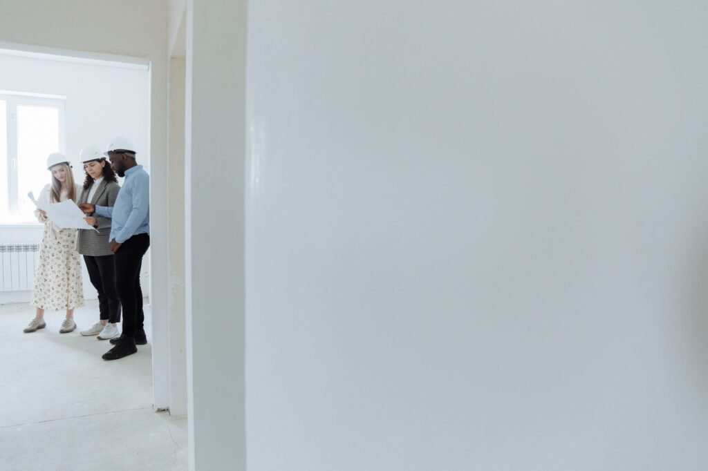 Architects wearing hard hats review blueprints inside a building under construction.