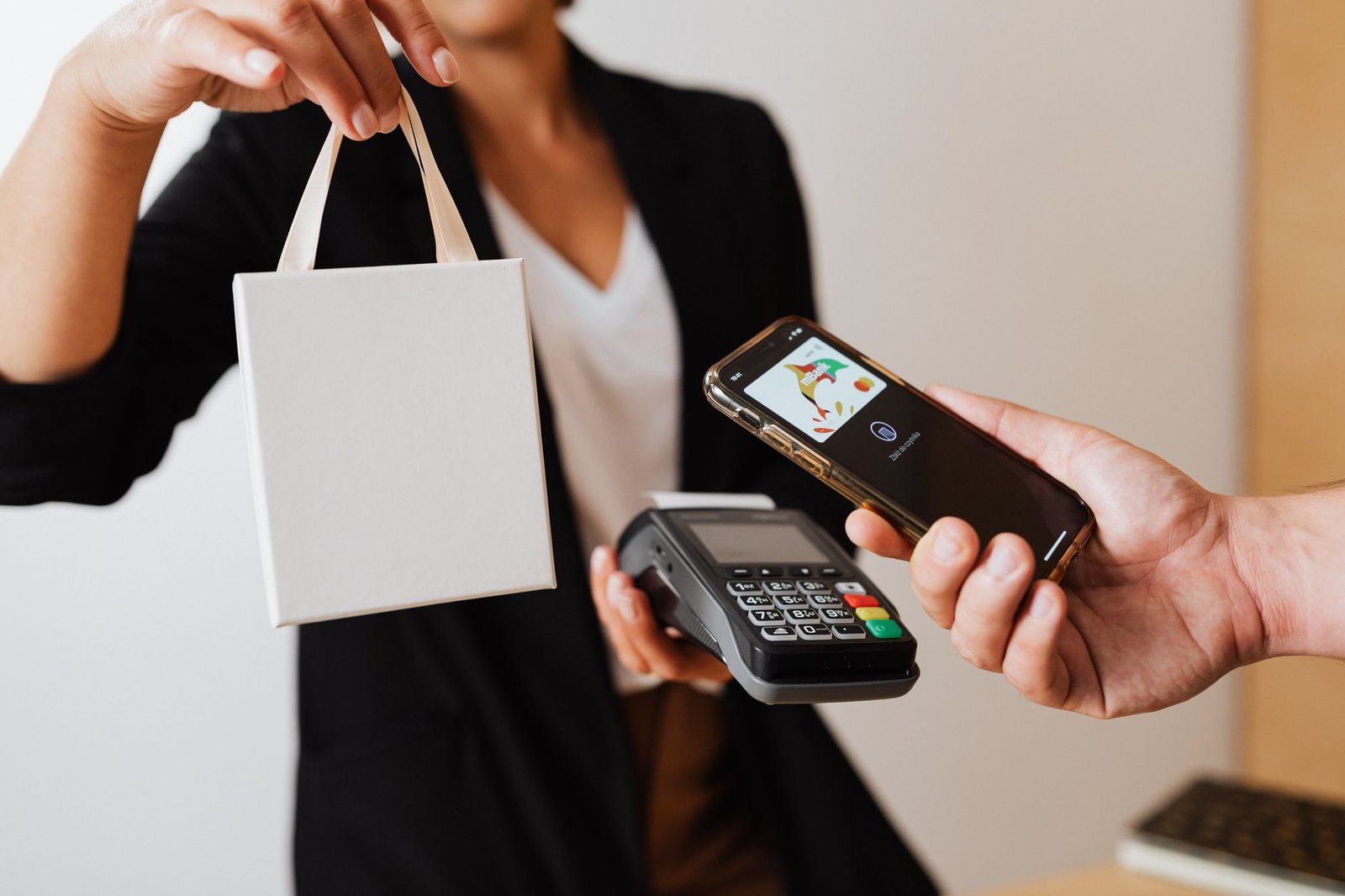 A person uses a smartphone for contactless payment with a payment terminal, while receiving a shopping bag.