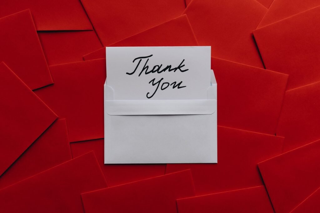 Elegant thank you card in white envelope on vibrant red envelopes flatlay. Perfect for gratitude themes.