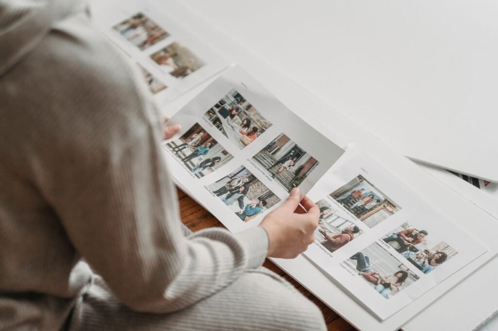 From above faceless person in warm gray clothes looking through printed images in album while sitting on floor