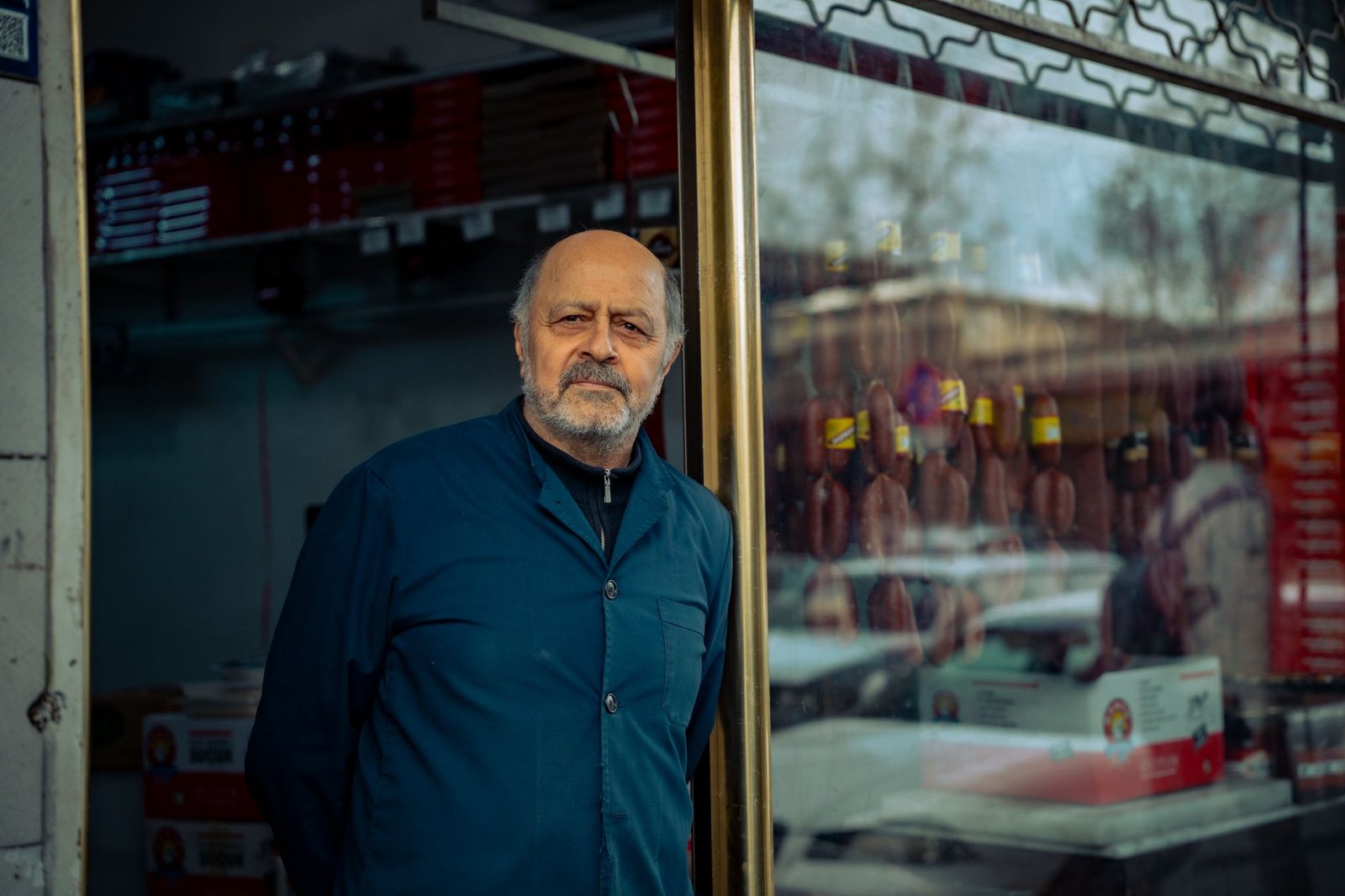 Senior man standing by his storefront in an urban area, showcasing a local business.
