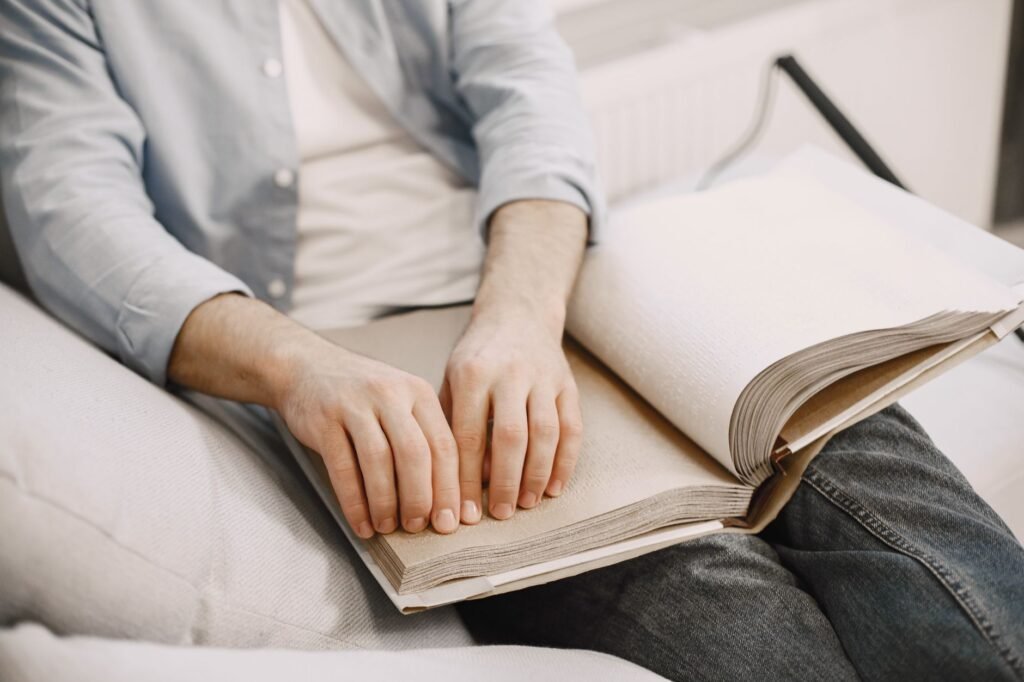 An adult reading a braille book indoors, highlighting visual impairment awareness.