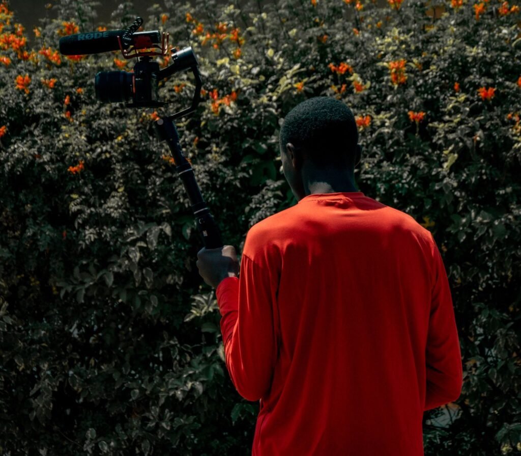 Back view of a man with a camera gimbal filming outdoors against a floral background.