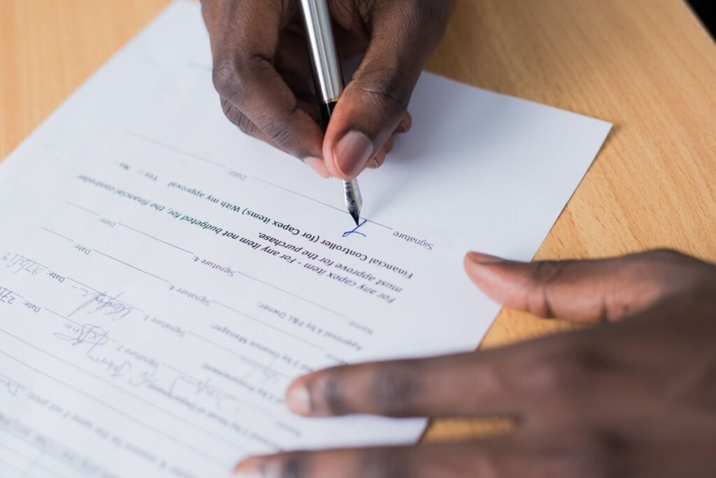 A close-up view of a person's hand signing a business contract on a desk with a pen.