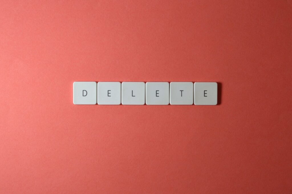 Close-up of keyboard letters spelling 'DELETE' on a coral background, emphasizing digital concepts.