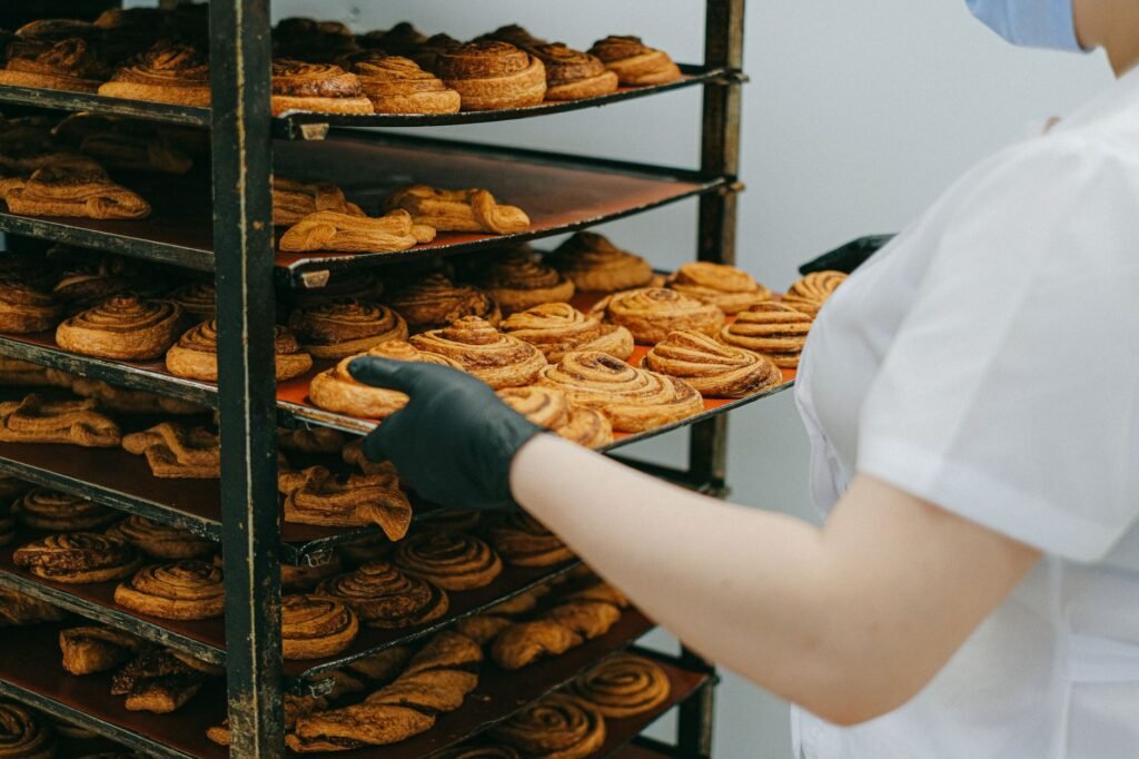 Baker placing freshly baked cinnamon rolls on a cooling rack in a bakery kitchen.