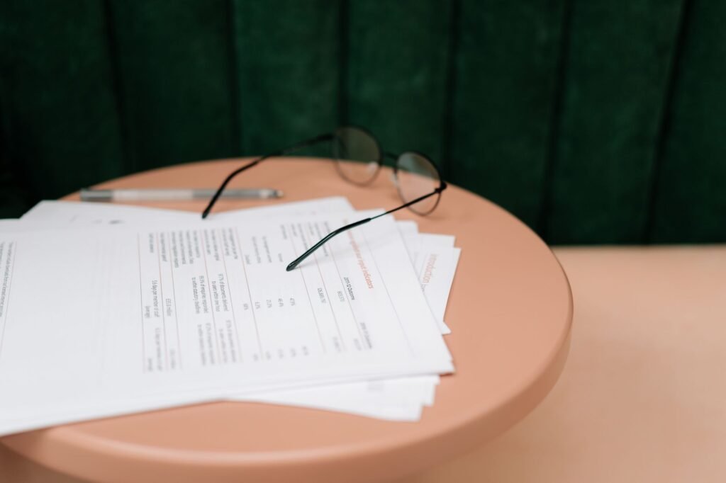 A close-up of documents, eyeglasses, and a pen on a round table indoors.