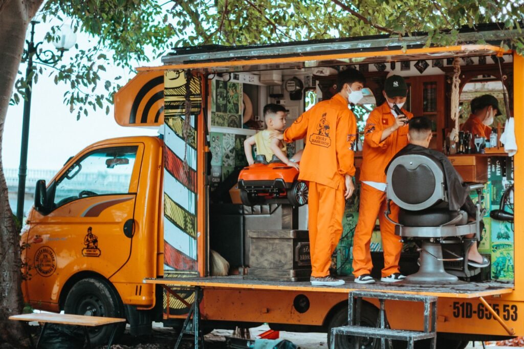 Street barbershop in an orange truck in Kon Tum, Vietnam, providing unique outdoor grooming.