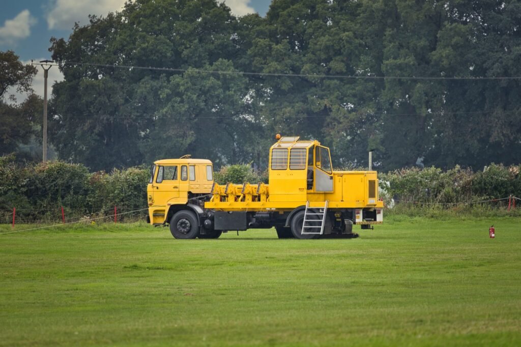 A distinctive yellow utility vehicle sits on a grassy field, ready for work.