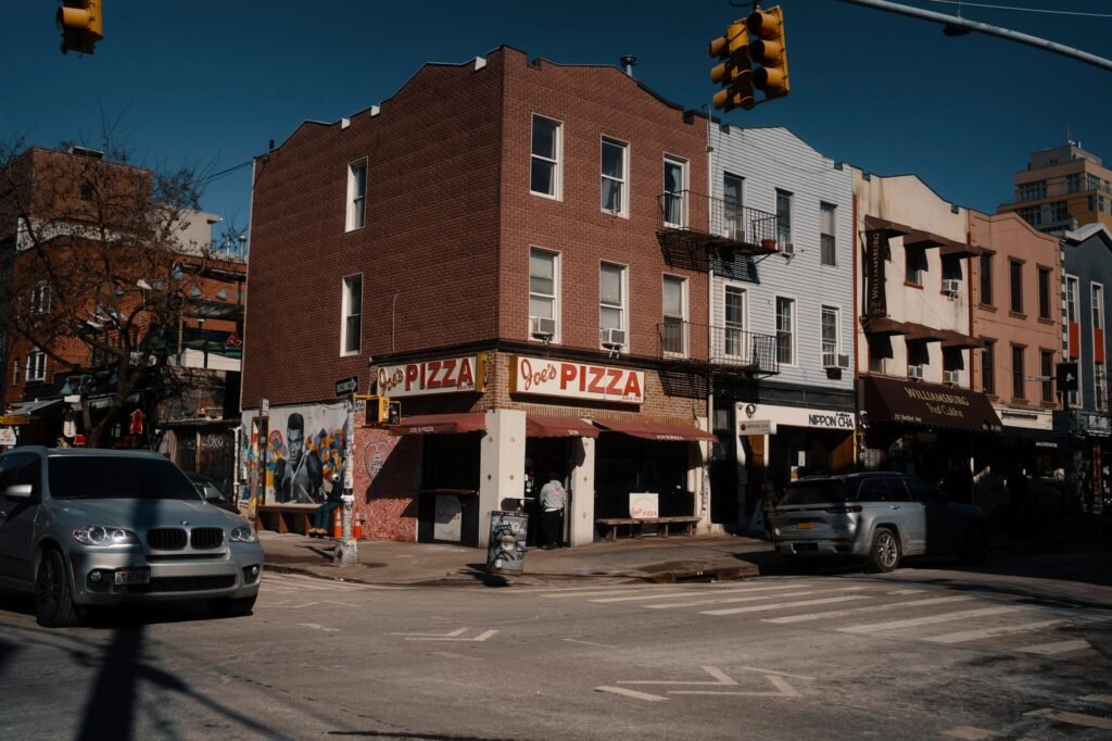 Street view of Joe's Pizza on a sunny day in Brooklyn, showcasing the lively urban atmosphere.