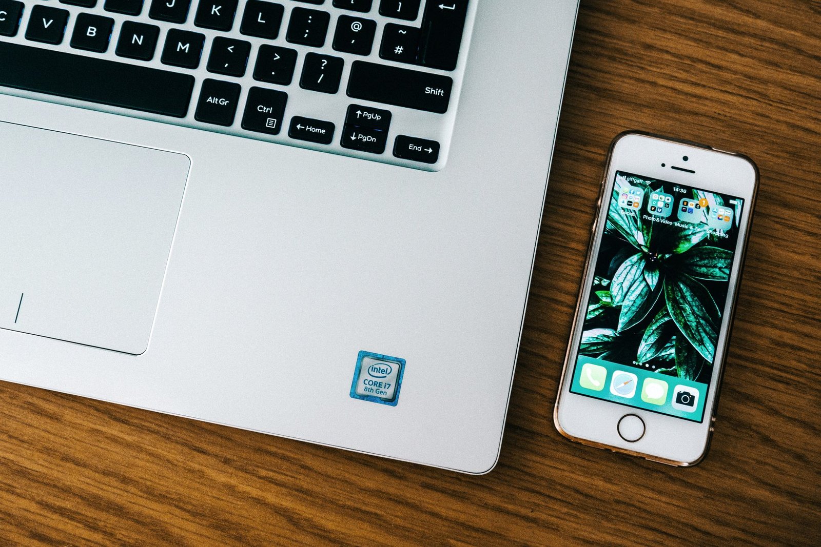 Close-up of a laptop and smartphone on a wooden desk in an office setting.