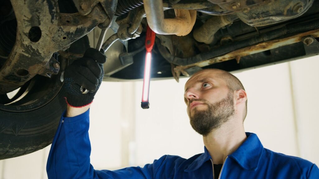 Mechanic focusing on vehicle maintenance under a car lift in a garage.